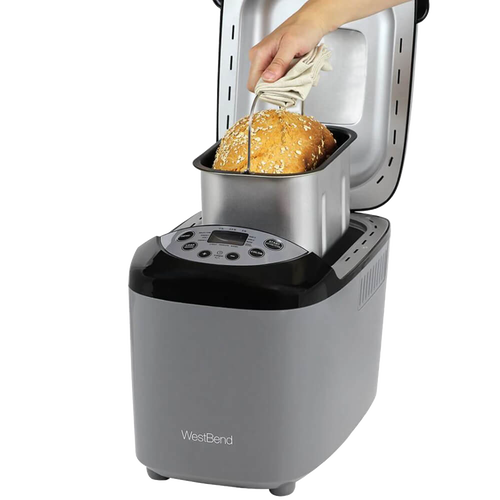 Hand removing freshly baked multigrain bread from a silver and black electric bread maker machine with digital controls, ideal for Kitchen & Food and Bread Making Supplies collections.