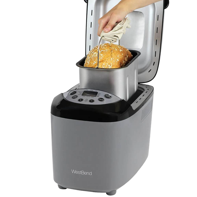 Hand removing freshly baked multigrain bread from a silver and black electric bread maker machine with digital controls, ideal for Kitchen & Food and Bread Making Supplies collections.