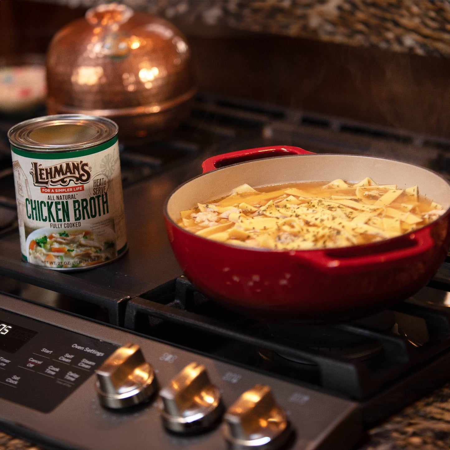 Lehman's canned chicken broth next to a red pot simmering homemade noodle soup on a stovetop, highlighting convenience for Farm, Garden & Tool, Kitchen & Food, and Emergency Supplies collections.