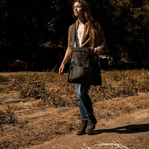 Person walking along a dry orchard path carrying a weather- and water-resistant charcoal gray harvesting bag with convertible straps, ideal for Farm, Garden & Tool and Apple Harvest Supplies collections.