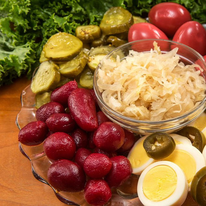 Clear glass bowl of tangy sauerkraut surrounded by sliced hard-boiled eggs topped with jalapeños, kidney beans, pickled cucumbers, grape tomatoes, and leafy greens, perfect for Kitchen & Food, Pantry, USA Made, Best Sellers, and Promo Eligible collections.