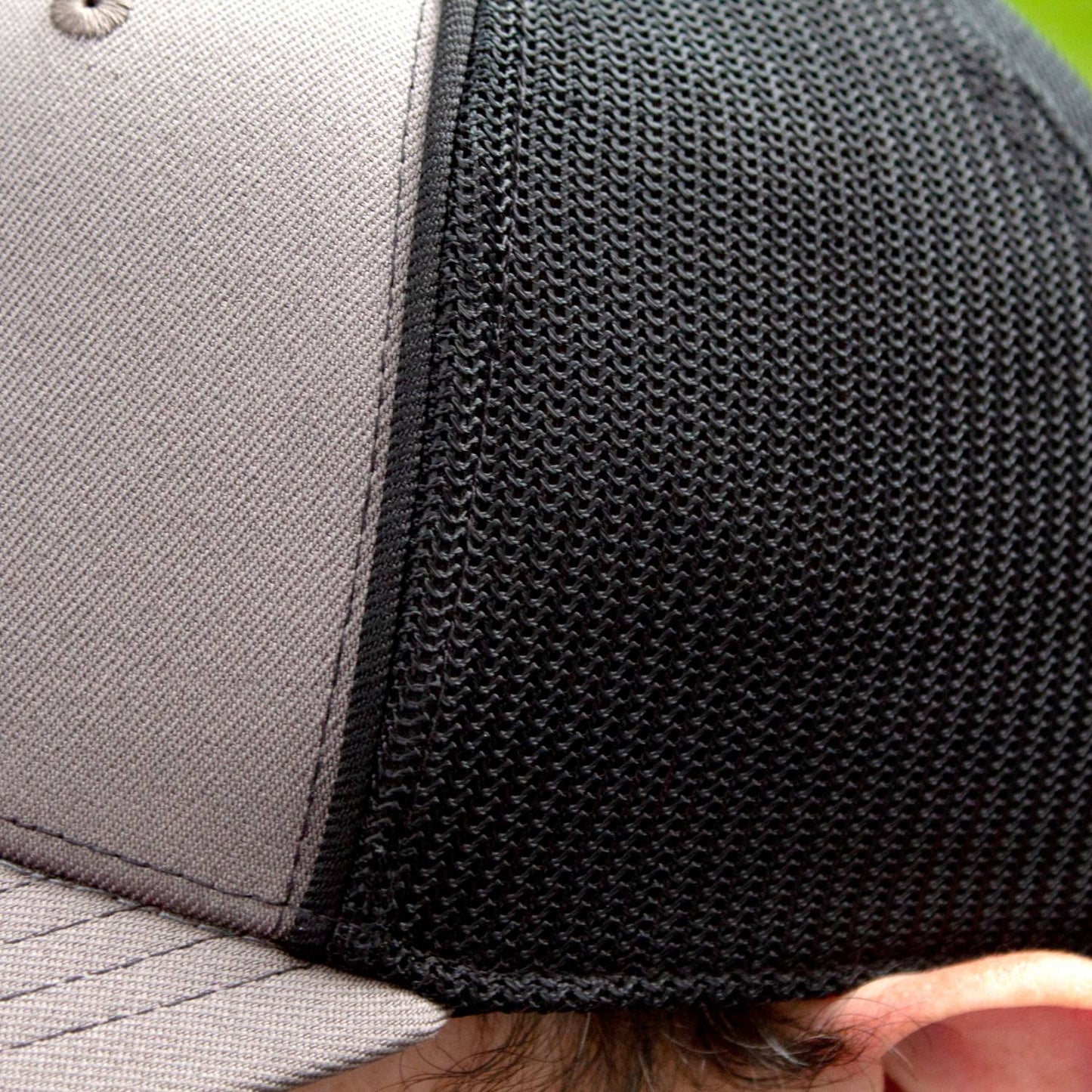 Close-up of a handcrafted trucker hat featuring a grey front panel with breathable black stretch mesh back, slightly pre-curved visor, and comfortable fit, ideal for Health & Wellness, Clothing and Accessories, Best Sellers, and Promo Eligible collections.