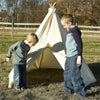 Two boys playing near a sturdy cream fabric teepee tent with six wooden poles set up outdoors on grass, showcasing a handcrafted, American-made child’s play hideout for outdoor and indoor fun.