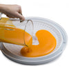 Hand pouring bright orange fruit puree onto a white drying sheet tray, preparing homemade fruit leather in Kitchen & Food and Food Preservation collections.