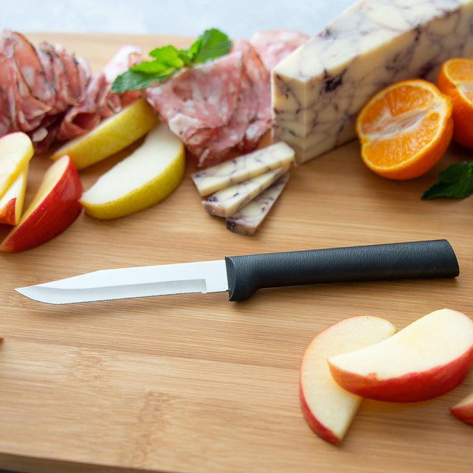 Handcrafted serrated paring knife with fine high carbon stainless steel blade and smooth black handle, made in USA, shown on wooden board with sliced apples, cheese, cured meat, and citrus, ideal for Kitchen & Food, Farm, Garden & Tool, and Knives & Axes collections.