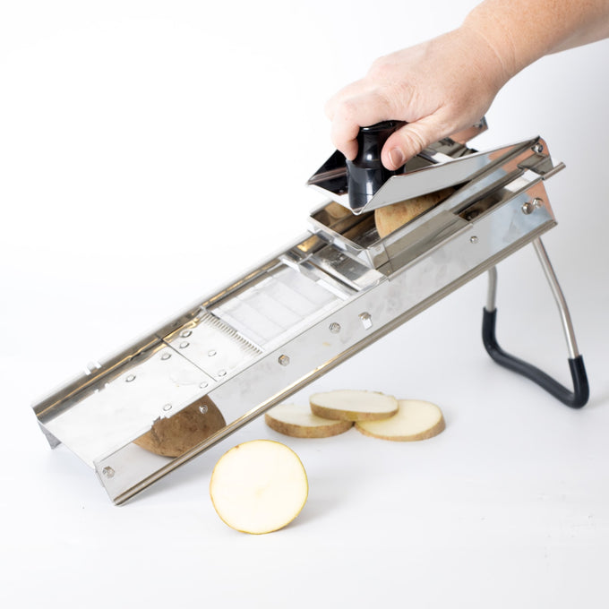 Handcrafted stainless steel mandoline slicer with foldable legs and safety holder slicing potato rounds, designed for precise food prep in Kitchen & Food and Food Prep collections.