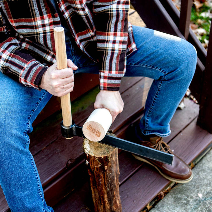 Person wearing plaid shirt and jeans demonstrating use of handcrafted Amish made froe and birch mallet on a wooden log, part of Farm, Garden & Tool and USA Made collections.