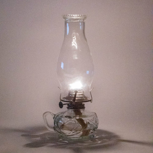 Handcrafted clear glass oil lamp with unique finger hold on the side, lit with warm flame, ideal for lamps & lighting, oil lamps, table lamps, and best sellers collections.