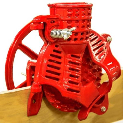 Handcrafted cast iron corn sheller in bright red with a large flywheel pulley clamped to a wooden surface, featured in Farm, Garden & Tool, Farm Tools, and Best Sellers collections.