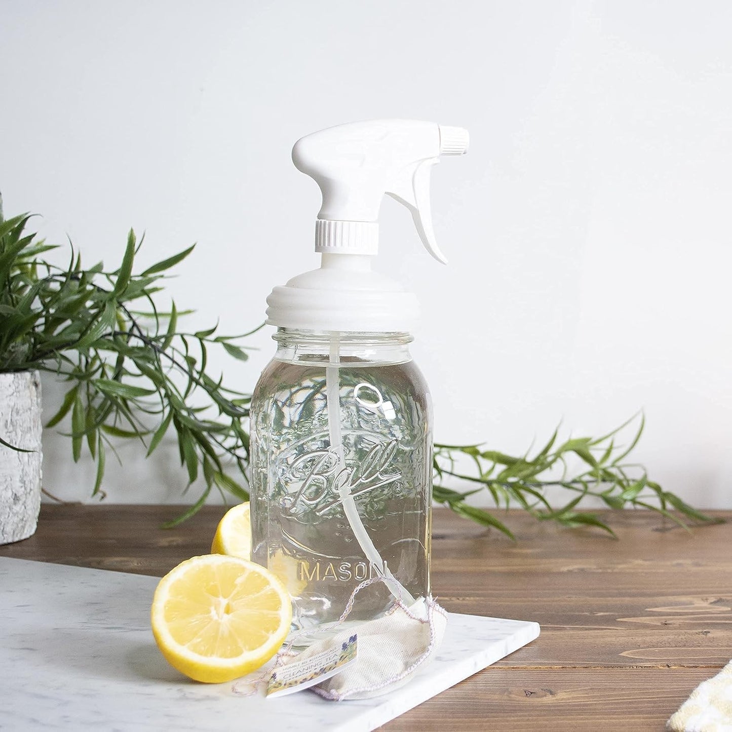 Clear regular-mouth mason jar with a white sprayer lid dispensing liquid, set on wooden surface near fresh lemon halves and green plant, part of Home & Decor, Household Helpers, USA Made, Best Sellers collections.