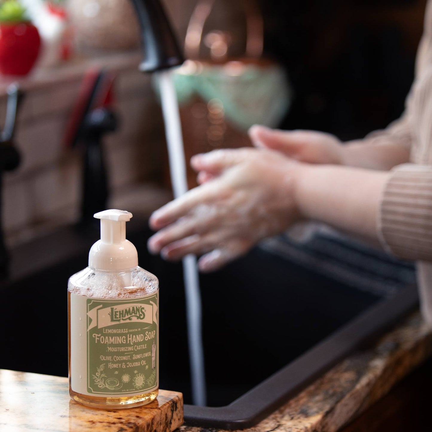 Clear pump bottle of Lehman's handcrafted moisturizing foaming hand soap with a natural formula featuring olive, coconut, sunflower, jojoba oils, and honey, made in USA, shown by a kitchen sink preparing for hand washing, perfect for Health & Wellness and Grooming collections.