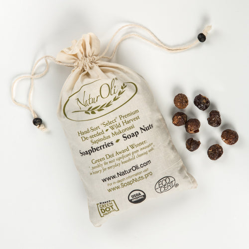Natural cotton drawstring bag labeled with eco certifications, filled with handcrafted soapberries spilling onto a white surface, featured in home, soapmaking, and laundry supplies collections.