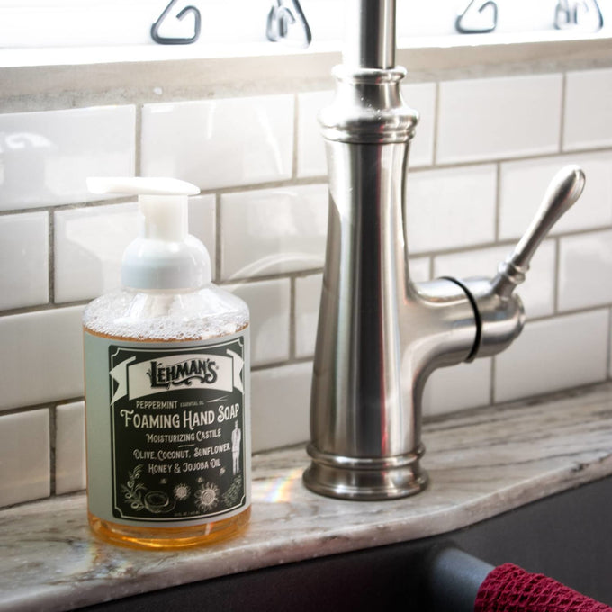 Lehman's handcrafted Peppermint foaming hand soap with moisturizing natural oils like olive, coconut, sunflower, honey, and jojoba, placed on a kitchen sink countertop, ideal for Health & Wellness and Grooming collections.