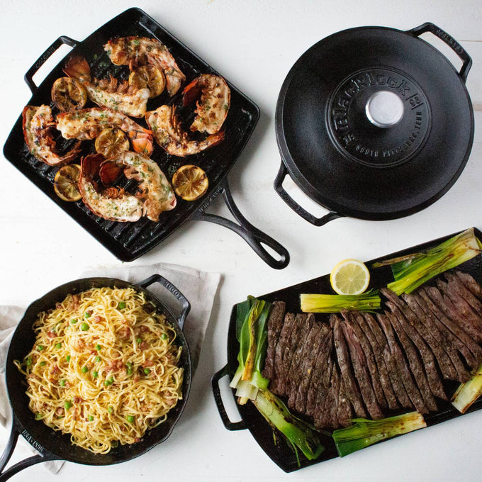 Assortment of cast iron cookware including a skillet with cooked noodles, a grill pan with grilled seafood and lemon slices, a griddle with sliced steak and green onions, and a seasoned cast iron lid, featured in Kitchen & Food, Cookware, Cast Iron, USA Made, and Best Sellers collections.