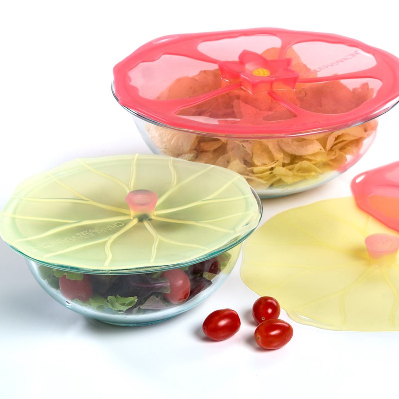Colorful reusable silicone bowl covers with lily pad and flower designs sealing glass bowls filled with salad and chips, featured in Kitchen & Food and Storage and Serving collections.