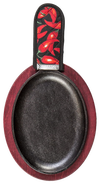 Oval cast iron griddle with a deep black cooking surface, set on a red stained wooden underliner and topped with a chili pepper patterned handle holder, ideal for camping and cookware collections.