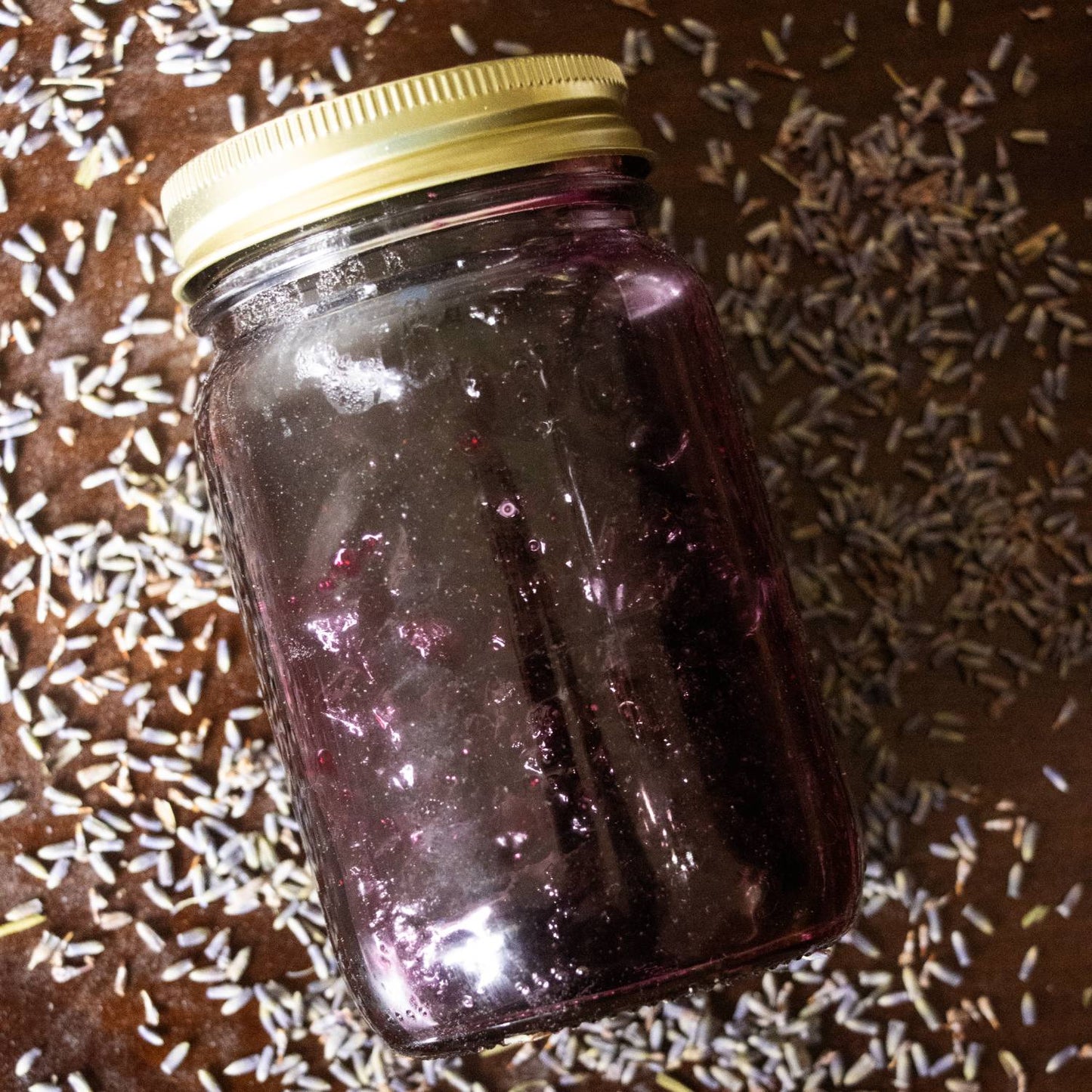 Clear American-made regular-mouth canning jar filled with dark preserved fruit and sealed with a golden lid, set on a surface scattered with dried lavender in Kitchen & Food collections.