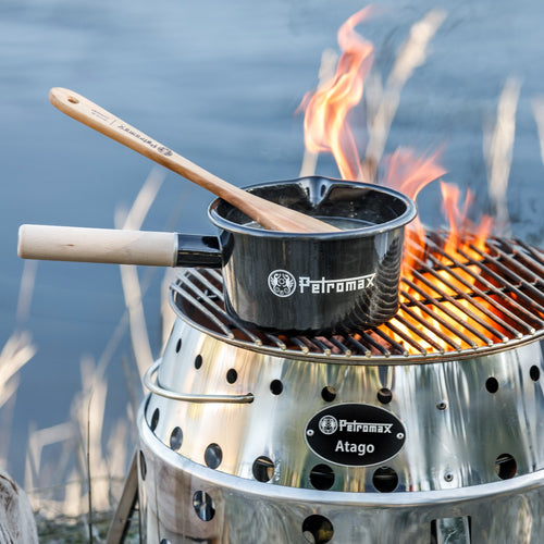 Black enamel Petromax pan with a light wooden handle cooking over an open flame on a stainless steel grill, ideal for camping and outdoor use in Farm, Garden & Tool and Cookware collections.