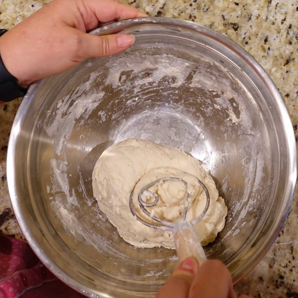 Handcrafted Amish made dough whisk with a smooth wooden handle and dual spiral metal wires mixing dough in a stainless steel bowl, ideal for Kitchen & Food and Baking Supplies collections.