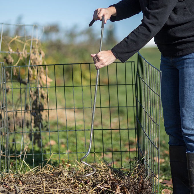 Person using a stainless steel compost mixer with a curved cushioned handle inside a wire compost bin outdoors on a sunny day, part of Farm, Garden & Tool, Composting, Garden Accessories, USA Made, and Best Sellers collections.