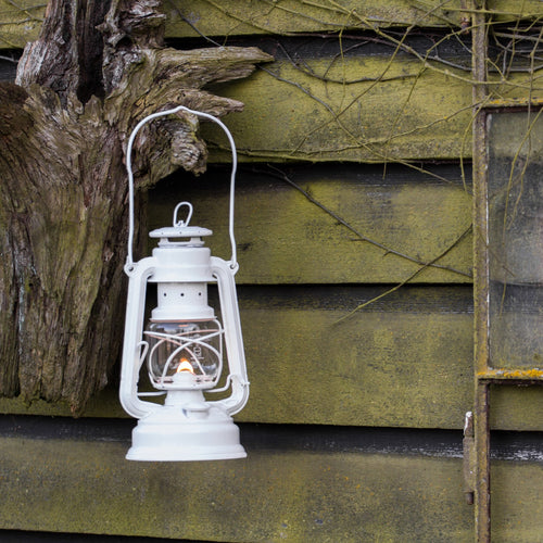Handcrafted white galvanized oil lantern with thermal heat-resistant SUPRAX globe softly lit, hanging on rustic moss-covered wood wall, ideal for Lamps & Lighting, Camping, Emergency Supplies, and outdoor use.