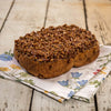 Large freshly baked pecan roll topped with chopped nuts and caramel glaze, resting on a floral cloth on rustic wooden surface, part of Kitchen & Food and USA Made collections