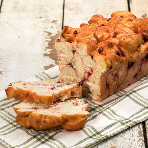 Handcrafted loaf of fresh cherry nut bread with swirls of cherry and pieces of walnut, made in USA, displayed on a green and white checkered cloth in Kitchen & Food collections.