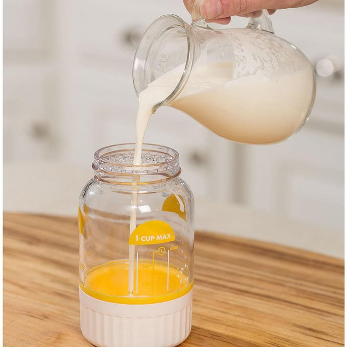Clear plastic butter maker jar with yellow measuring markings being filled with heavy whipping cream from a glass pitcher, designed for easy homemade butter preparation in Farm, Garden & Tool and Kitchen & Food collections.