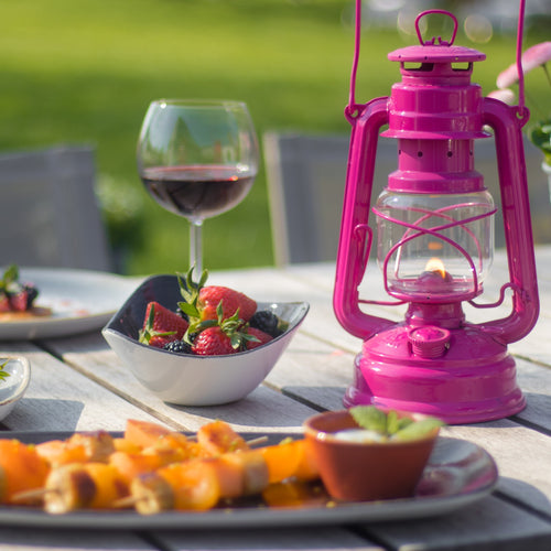 Handcrafted bright pink galvanized oil lantern with thermal heat-resistant globe, glowing warmly on an outdoor wooden table set with fresh berries, wine, and appetizers, perfect for Lamps & Lighting, Camping, Emergency Supplies, and Outdoor collections.
