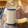 Hand holding a handcrafted stoneware mug with two blue stripes and a long handle on a kitchen countertop, featured for Kitchen & Food, Dinnerware, USA Made, and Best Sellers collections.