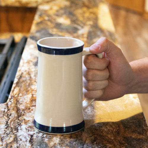 Hand holding a handcrafted stoneware mug with two blue stripes and a long handle on a kitchen countertop, featured for Kitchen & Food, Dinnerware, USA Made, and Best Sellers collections.