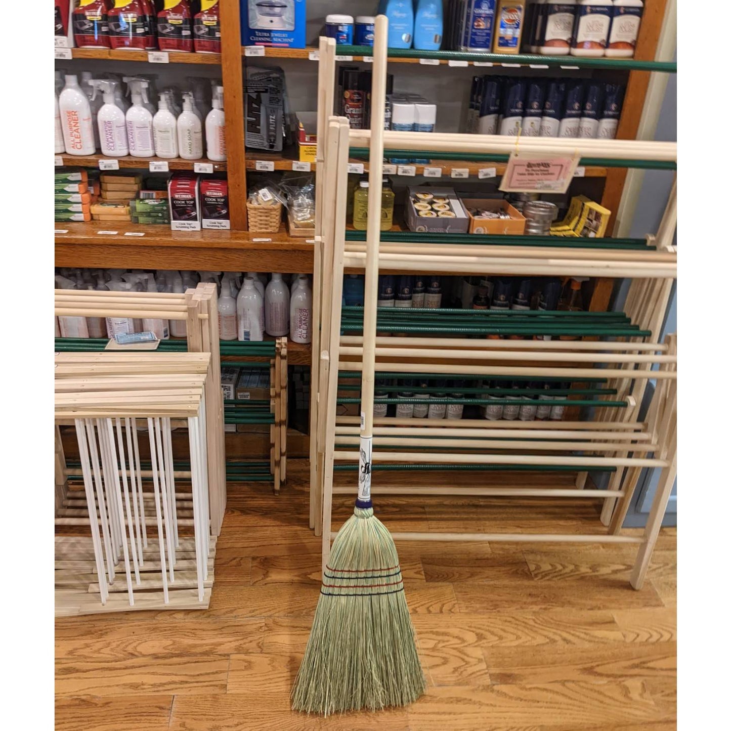 Handcrafted Amish made broom with natural corn straw bristles and a wrapped wooden handle, standing on hardwood floor among wooden drying racks, ideal for Home & Decor and Household Cleaning.