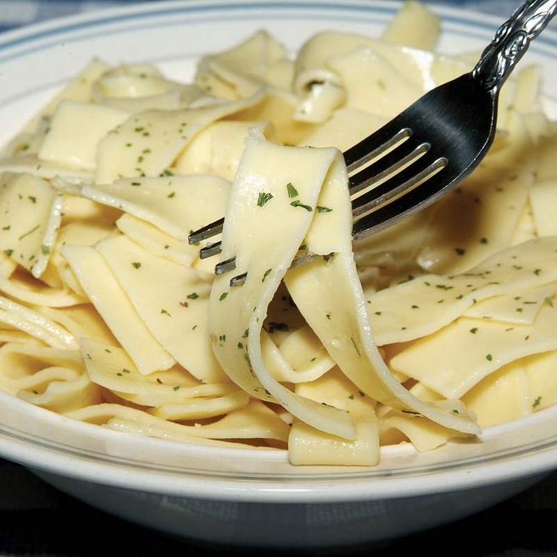 Close-up of a fork twirling wide, handcrafted egg noodles sprinkled with herbs in a white bowl, part of Kitchen & Food, Pantry, USA Made, Best Sellers, and Promo Eligible collections.