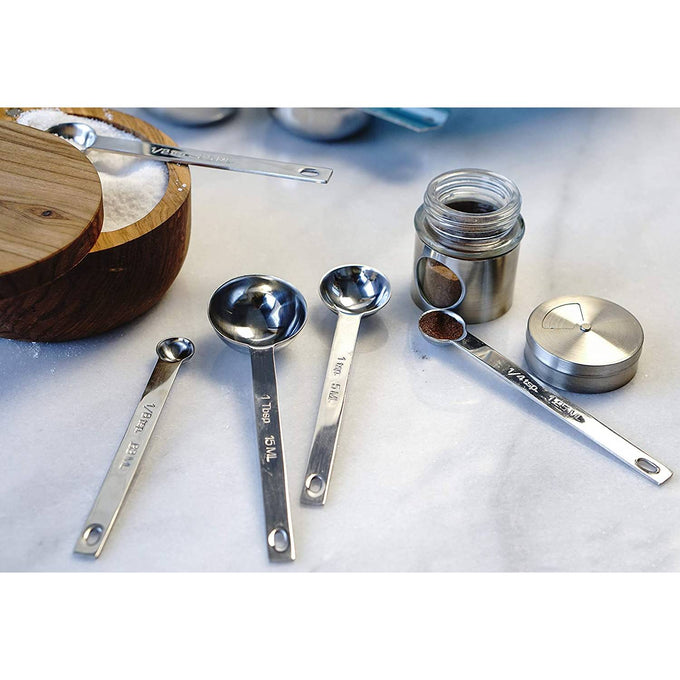 Set of five linked stainless steel measuring spoons with clearly marked sizes ranging from 1/8 teaspoon to 1 tablespoon, displayed alongside a small jar of ground spice, ideal for precise food prep in kitchen and measuring collections.