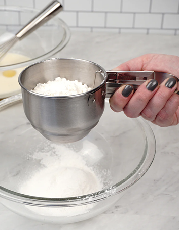 Stainless steel vintage-style flour sifter with easy one-handed operation, dishwasher safe, held over glass mixing bowl in Kitchen & Food, Baking Supplies, and Cookware collections.