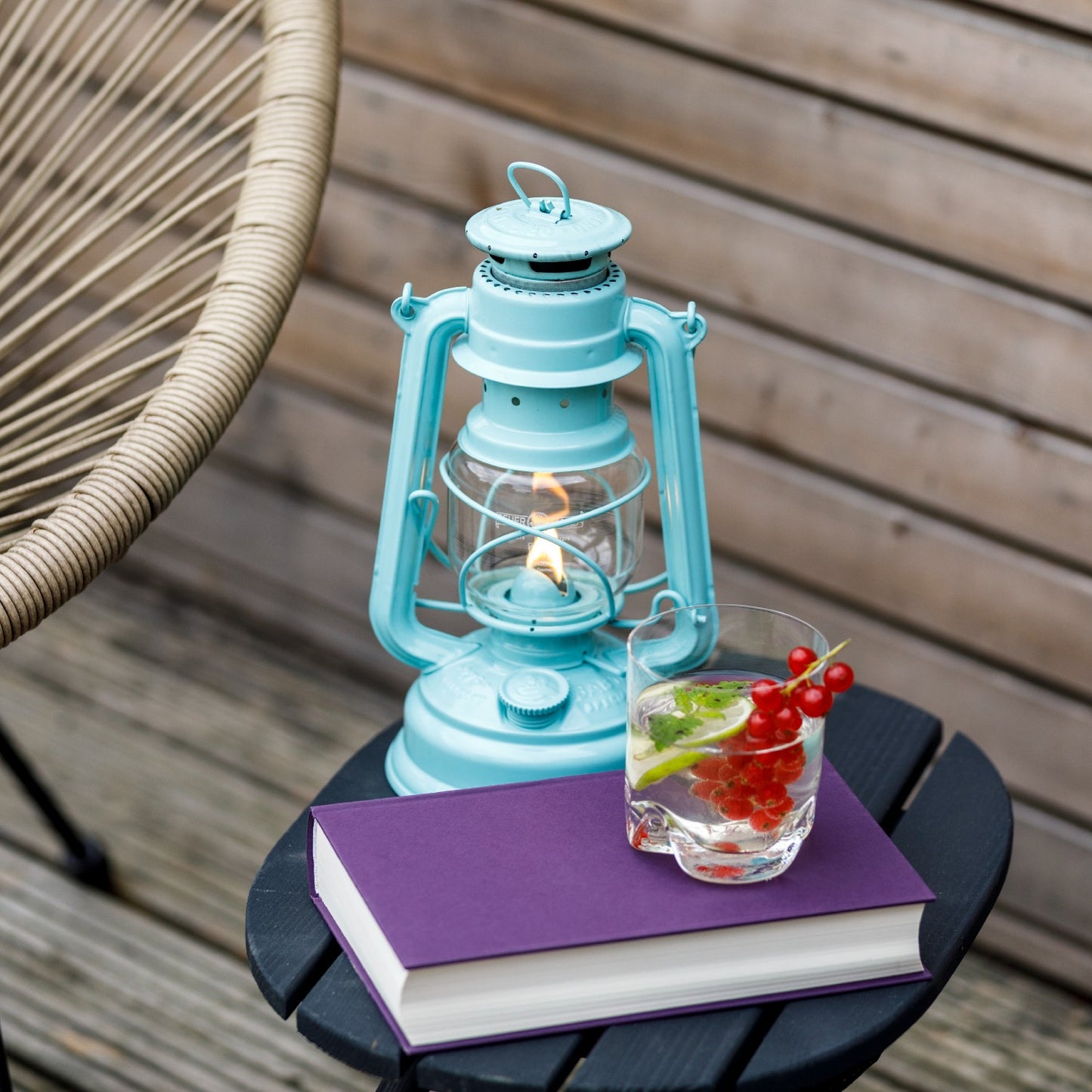 Handcrafted turquoise galvanized oil lantern glowing softly with a thermal heat-resistant globe, displayed on a small black table with a purple book and a glass of water, ideal for Lamps & Lighting, Camping, and Emergency Supplies collections.