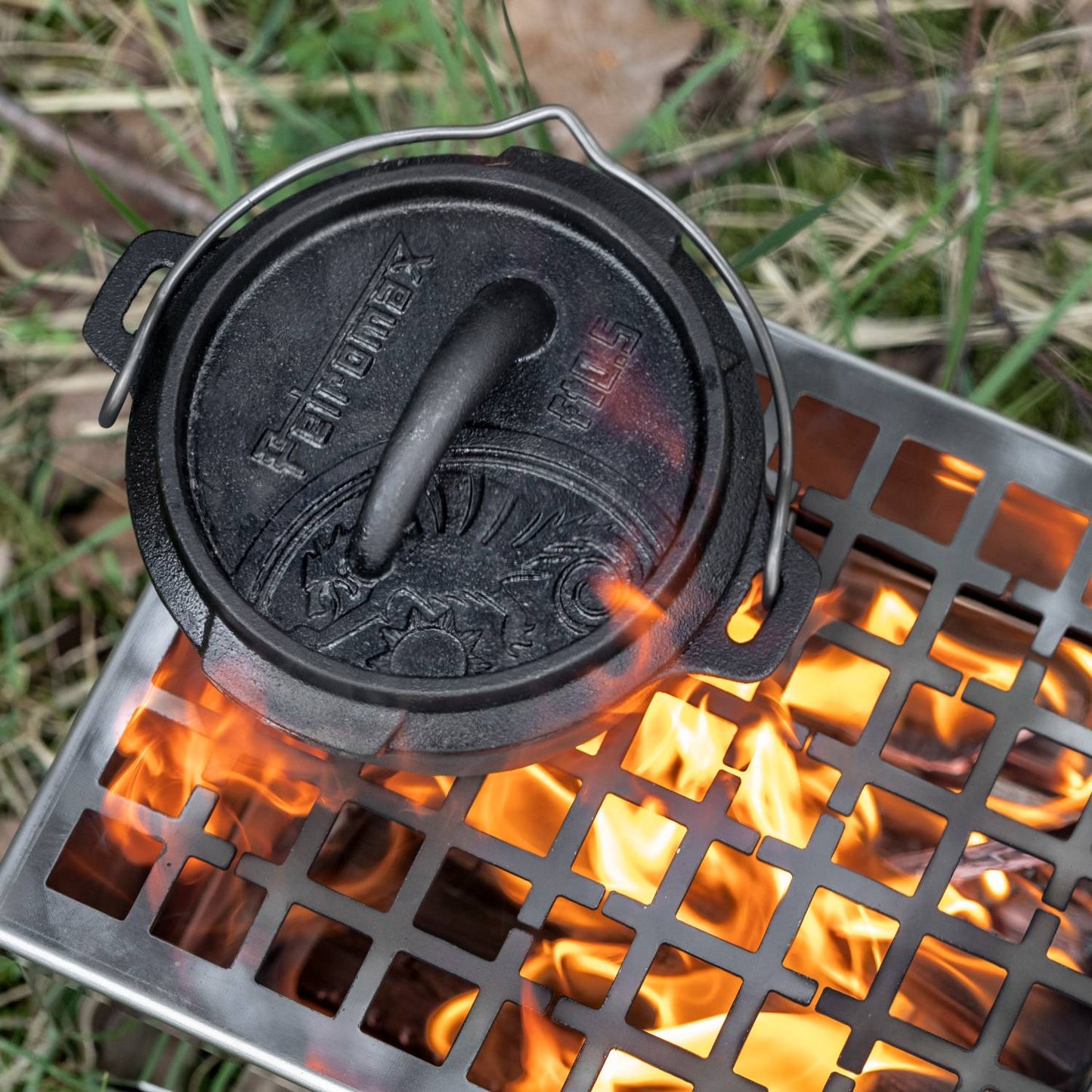 Cast iron Dutch oven with flat base and embossed lid featuring a sturdy handle, cooking over an open flame on a metal grill, ideal for Kitchen & Food, Cookware, Cast Iron, Best Sellers, and Promo Eligible collections.