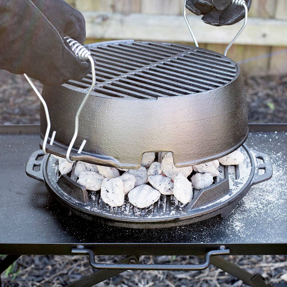 Gloved hands lifting a portable 12-inch cast iron grill lid with handles, showing hot charcoal briquettes underneath on a sturdy outdoor camping stove, handcrafted and made in USA.