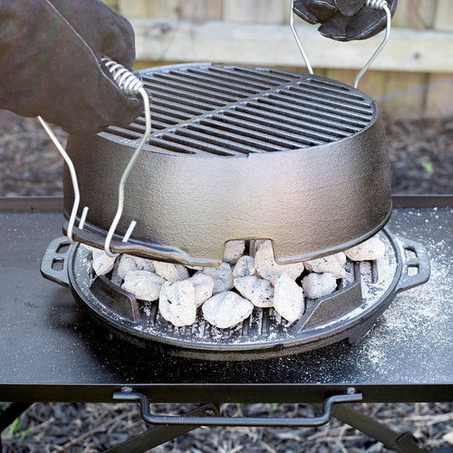Gloved hands lifting a portable 12-inch cast iron grill lid with handles, showing hot charcoal briquettes underneath on a sturdy outdoor camping stove, handcrafted and made in USA.