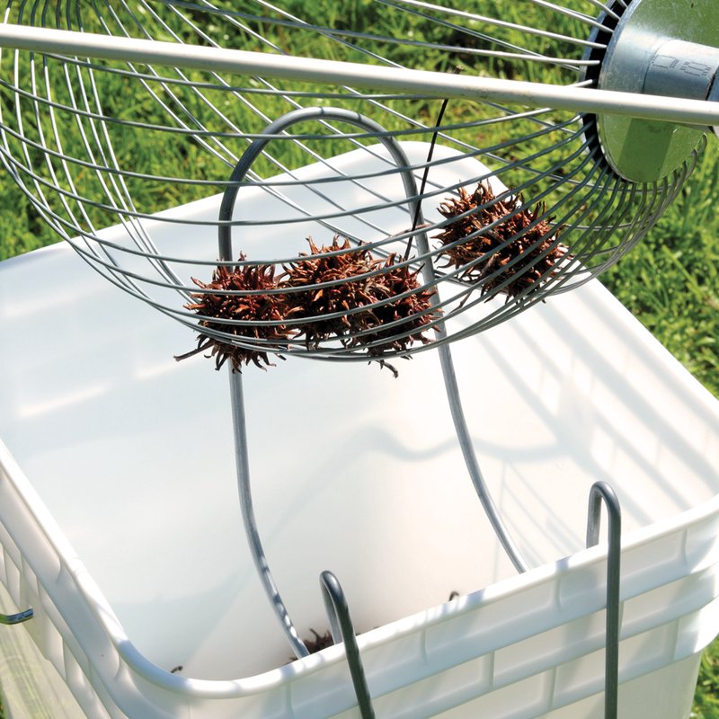 Metal wire nut gatherer lifting sweet gum seed pods above a white collection container, designed for easy yard cleanup with minimal bending; featured in Farm, Garden & Tool, Lawncare, Best Sellers, and Promo Eligible collections.