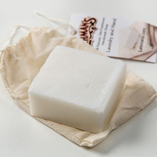 Handcrafted white natural laundry and hand soap bar made from organic coconut oil, resting on a cloth pouch with product information card, highlighting USA made, health, and grooming collections.