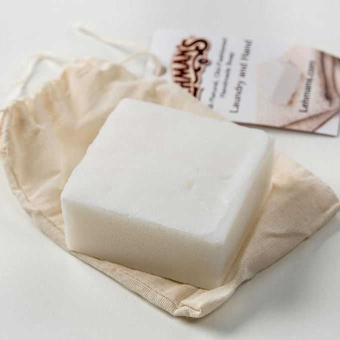 Handcrafted white natural laundry and hand soap bar made from organic coconut oil, resting on a cloth pouch with product information card, highlighting USA made, health, and grooming collections.