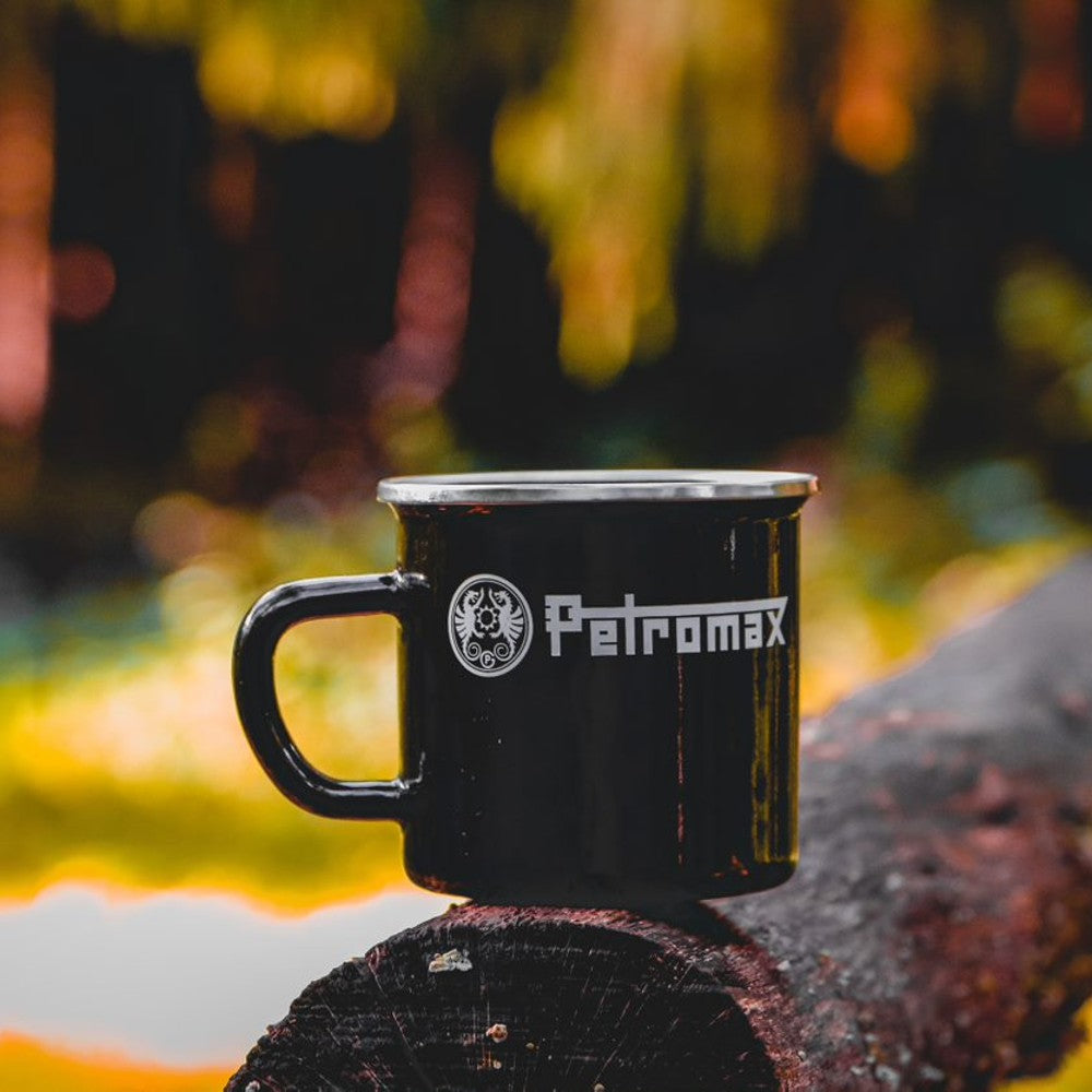 Black enameled steel mug with metal rim and white logo, resting on a weathered log outdoors, perfect for Farm, Garden & Tool, Camping, Brewing Coffee and Tea, and Kitchen & Food collections.