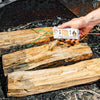 Hand holding a pull string fire starter pack with green ignition cords, placed over dry wood logs in a fire pit, ideal for Farm, Garden & Tool and Camping collections.