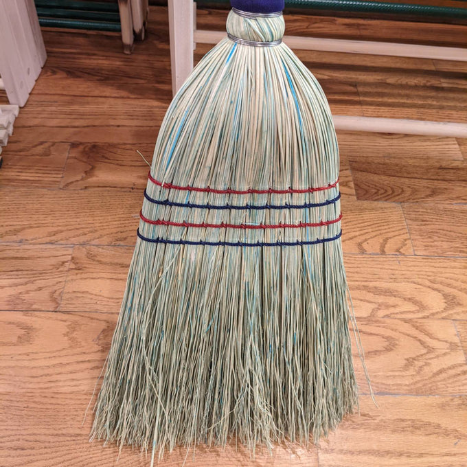Handcrafted Amish-made corn straw broom with tightly bound natural bristles in red and blue stitching, resting on hardwood floor, perfect for household cleaning and Home & Decor.