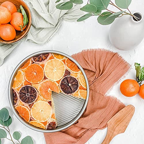 Round aluminized steel cake pan with fluted surface featuring a citrus-topped cake, styled with natural kitchen textiles and greenery, perfect for Kitchen & Food and Cookware collections.
