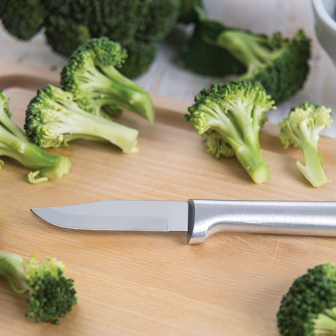 Paring knife with a sharp carbon stainless steel blade and satin-finished cast aluminum handle resting on a wooden cutting board surrounded by fresh broccoli, ideal for kitchen food prep in USA made and best sellers collections.