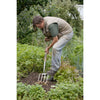 Gardener using a Spear & Jackson Traditional Stainless Digging Fork with mirror-polished stainless steel tines and weatherproof hardwood handle to break soil in a vegetable garden, ideal for farm, garden, and lawncare tasks.