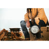 Person wearing outdoor gloves and jacket holding a handcrafted cast iron Bucking Bronco combo cooker near a campfire with wood logs and cooking pot, featured in Kitchen & Food, Cast Iron, USA Made, and Best Sellers collections.