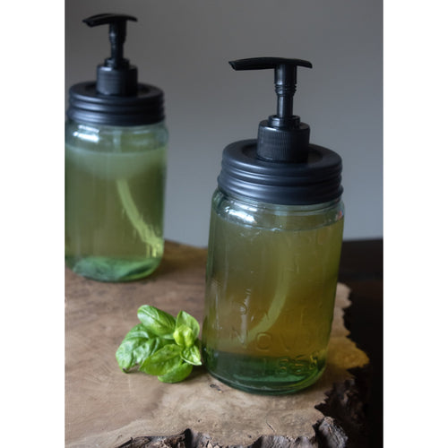 Black pump lids with dispensing tubes fitted on clear regular-mouth glass jars filled with liquid soap, displayed on a rustic wooden surface with fresh basil, highlighting USA made and eco-friendly Health & Wellness, Home & Decor, and Household Helpers collections.